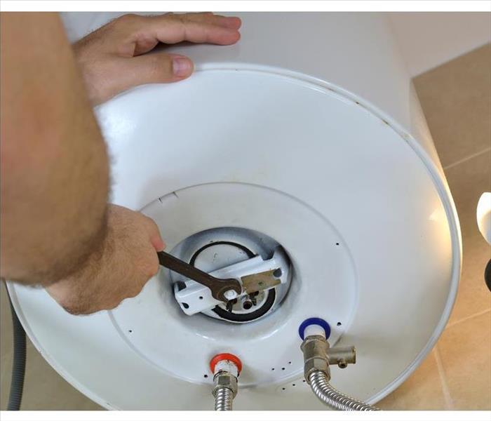 Man's hands unscrewing a threaded nut on a water heater with a wrench in a boiler